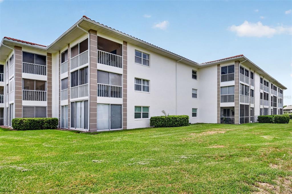 A multi-story apartment building with white stucco walls, screened balconies, and a green lawn — 6505 STONE RIVER ROAD UNIT 308, BRADENTON, FL