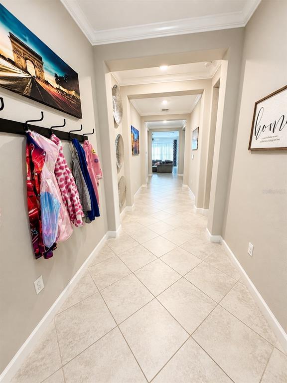 A hallway with light-colored tile floors leads to a living area with hanging coats displayed — 11614 SUNBURST MARBLE ROAD, RIVERVIEW, FL