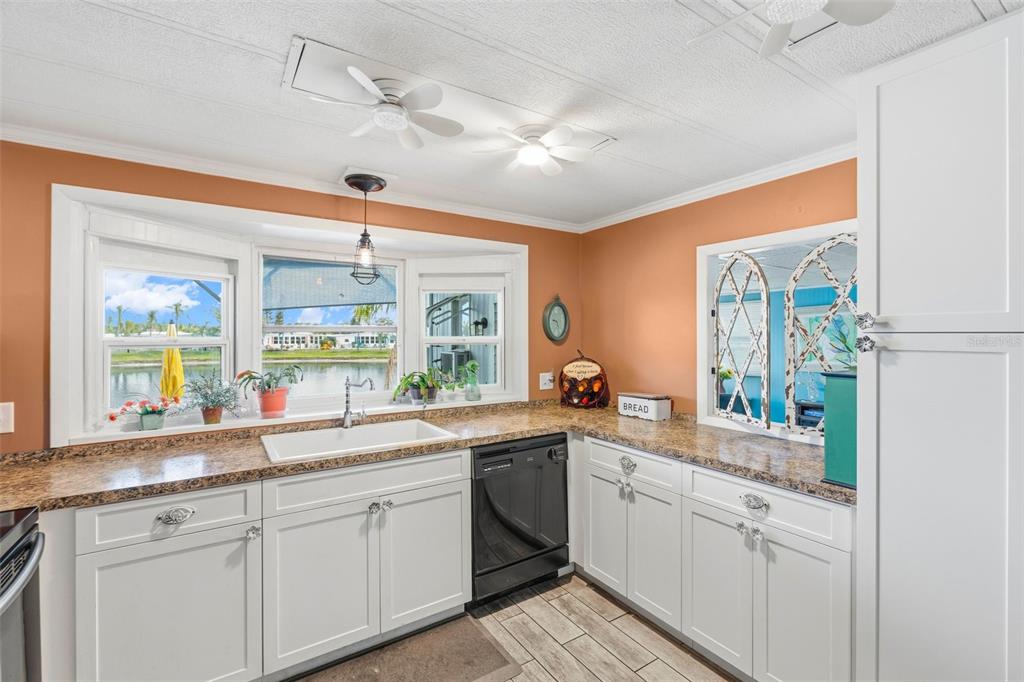 A kitchen features white cabinets, granite countertops, a black dishwasher, and a bay window view — 970 JOLANDA CIRCLE, VENICE, FL