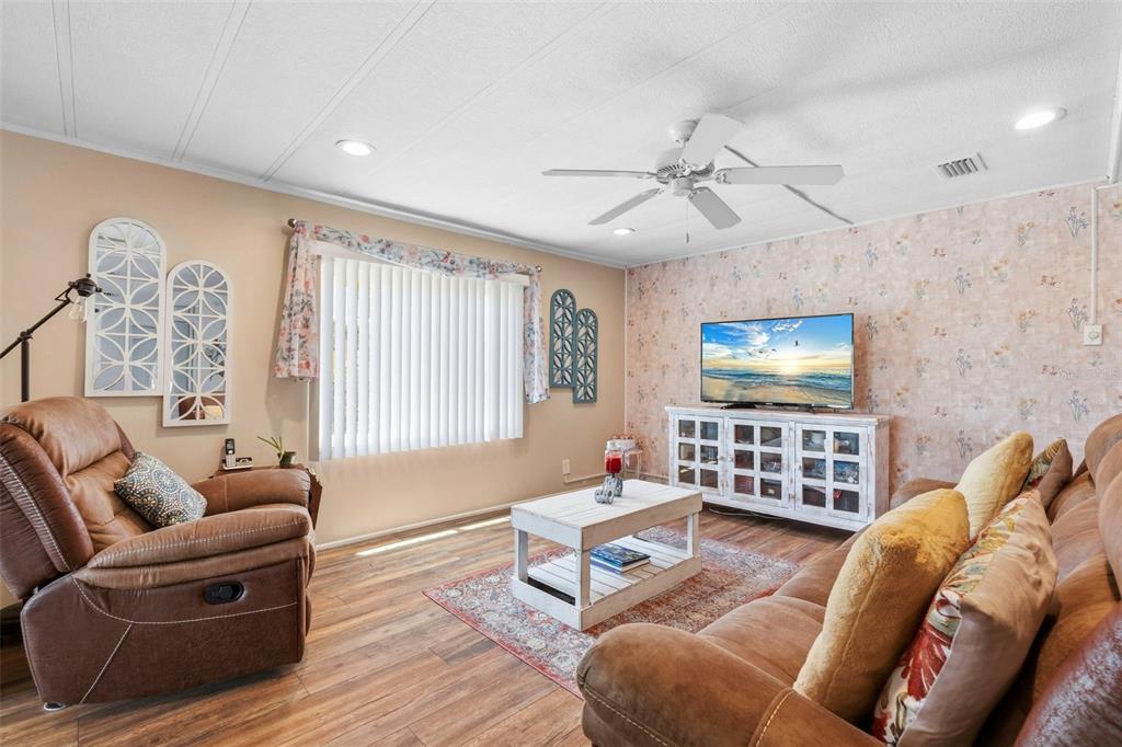 A living room features wood-look flooring, a floral wallpaper accent wall, and a ceiling fan — 970 JOLANDA CIRCLE, VENICE, FL