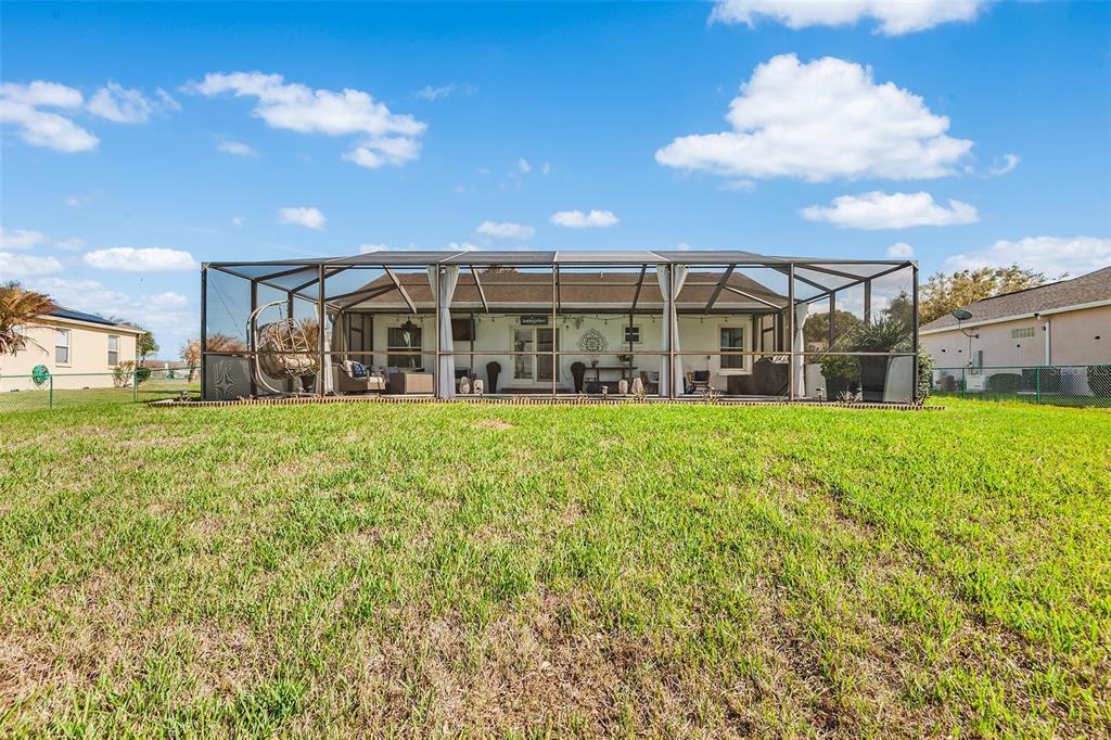 A screened-in patio overlooks a grassy backyard under a blue sky with scattered clouds — 4367 DINNER LAKE BOULEVARD, LAKE WALES, FL