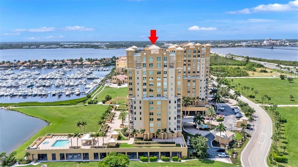 An aerial view shows a tall, tan residential building situated next to a boat marina — 140 RIVIERA DUNES WAY UNIT 503, PALMETTO, FL