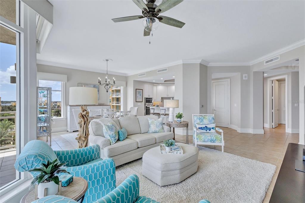 A bright living room features light-colored furniture, a patterned armchair, and a view of palm trees — 140 RIVIERA DUNES WAY UNIT 503, PALMETTO, FL