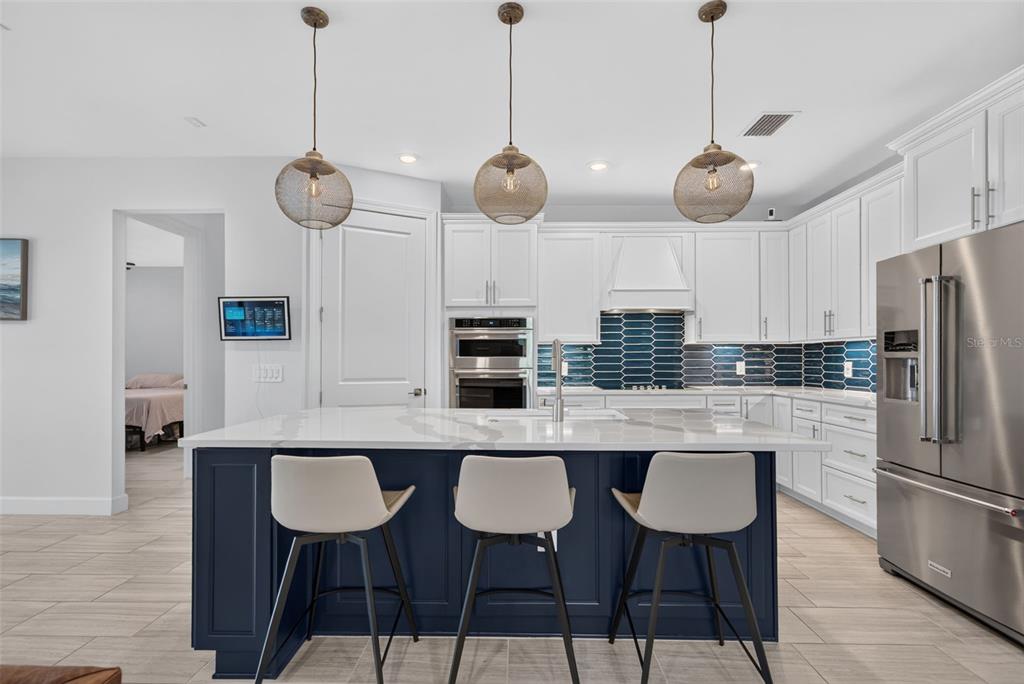 A kitchen with a blue island, white cabinets, stainless steel appliances, and three pendant lights — 704 PINTAIL COVE, BRADENTON, FL