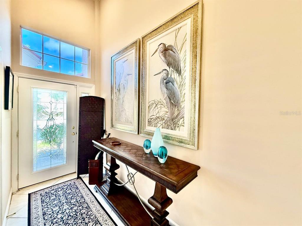 An entryway features a wooden console table, two heron prints, and a glass-paneled front door — 1605 SAND KEY ESTATES COURT, CLEARWATER, FL