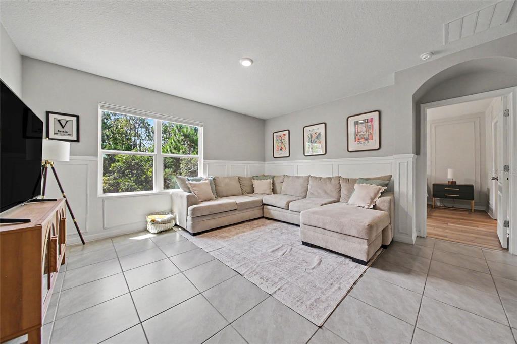 A living room features a large sectional sofa, wainscoting, tile flooring, and three framed prints — 6708 ALDER RD, HARMONY, FL
