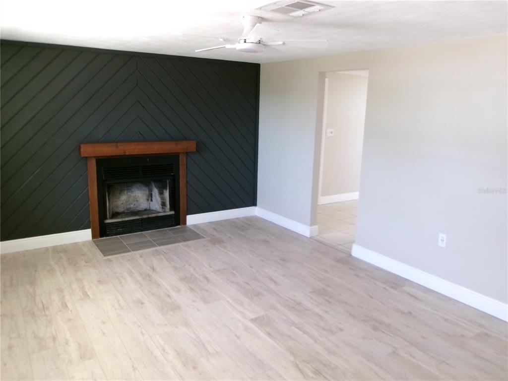 A living room features light wood-look flooring, a dark chevron-patterned accent wall, and a fireplace — 5103 VALIMOR DRIVE, HOLIDAY, FL