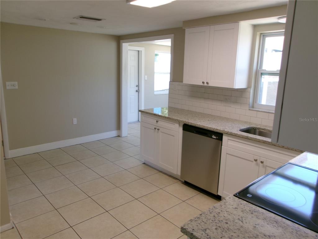 A kitchen features white cabinets, granite countertops, a stainless steel dishwasher, and beige tile flooring — 5103 VALIMOR DRIVE, HOLIDAY, FL