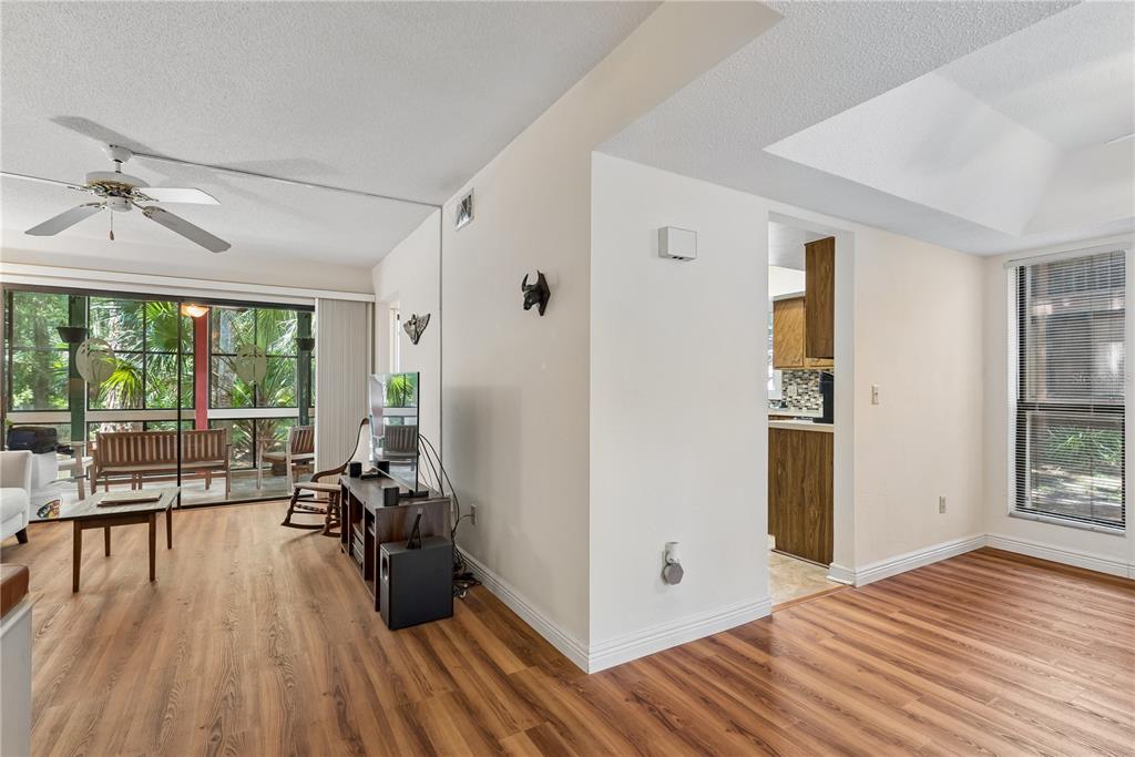 A living room with wood-look flooring leads to a screened porch and a kitchen doorway — 35 FAIRWAYS CIRCLE UNIT 35, PALM COAST, FL