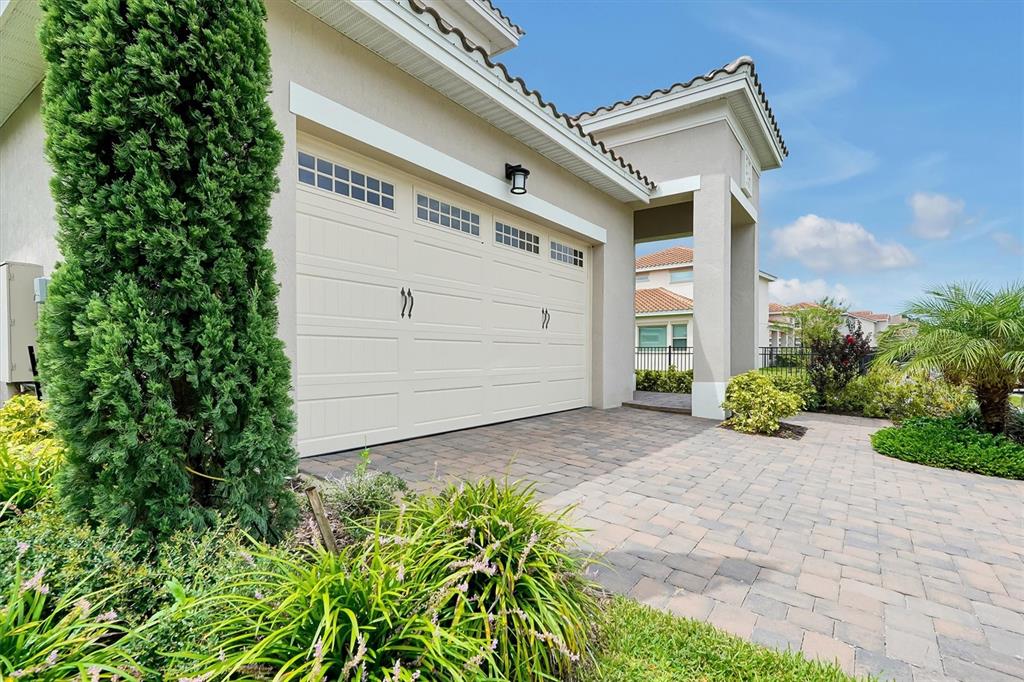 A beige house exterior features a two-car garage, a paved driveway, and landscaped greenery — 13342 BROMBOROUGH DRIVE, ORLANDO, FL