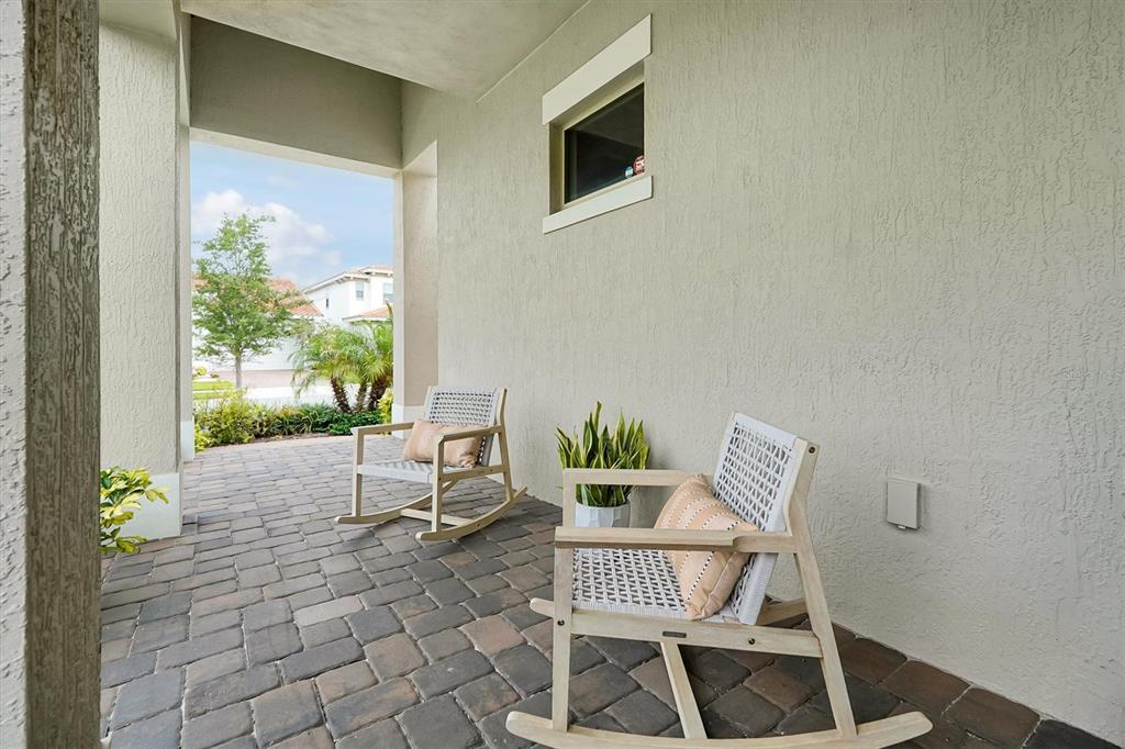 Two rocking chairs sit on a paved patio beneath a covered porch with stucco walls — 13342 BROMBOROUGH DRIVE, ORLANDO, FL