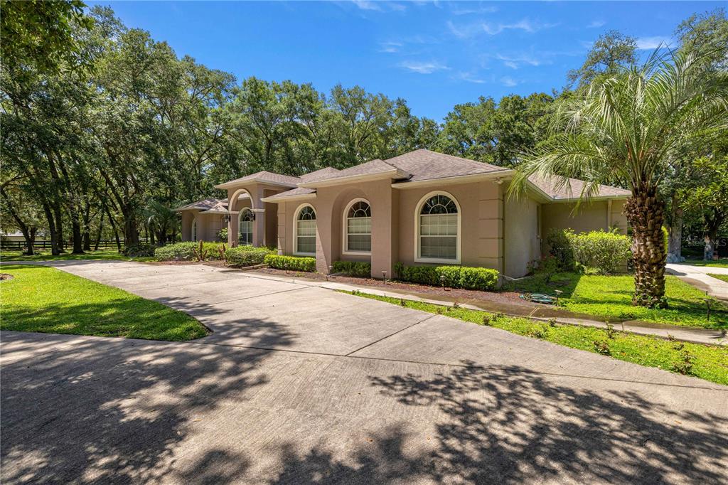 A single-story stucco house with arched windows and a concrete driveway sits among trees — 7305 SW 86TH LANE, OCALA, FL