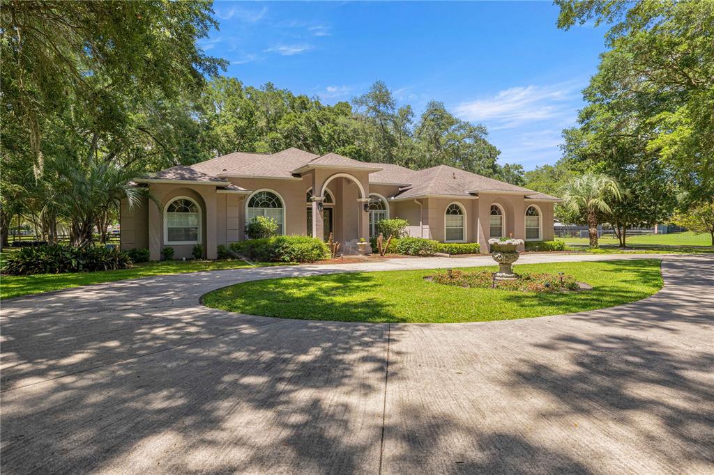 A single-story tan house with a circular driveway and a central fountain in the yard — 7305 SW 86TH LANE, OCALA, FL