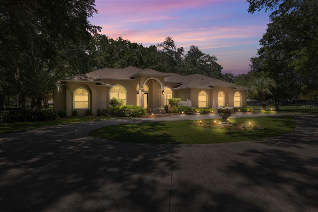 A single-story house with a circular driveway and arched windows at dusk — 7305 SW 86TH LANE, OCALA, FL