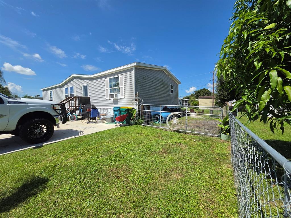 A light-gray manufactured home with a side yard, chain-link fence, and a parked truck — 1837 BLOSSOM COURT, PUNTA GORDA, FL
