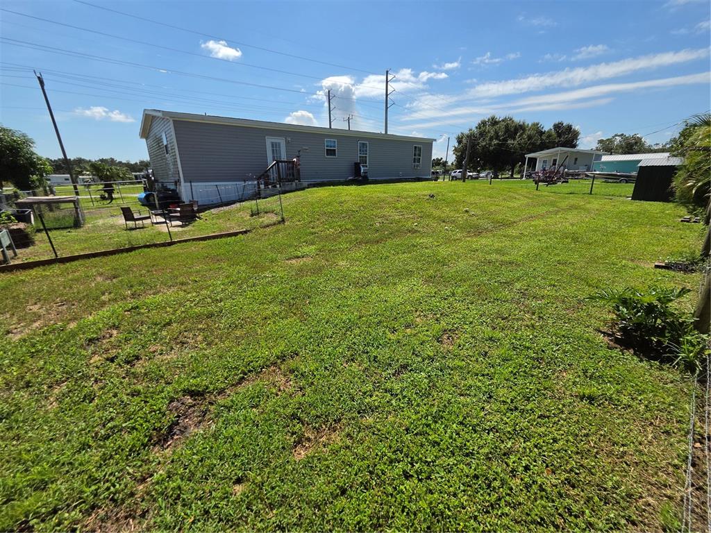 A grassy backyard view of a single-wide mobile home with a small wooden deck — 1837 BLOSSOM COURT, PUNTA GORDA, FL