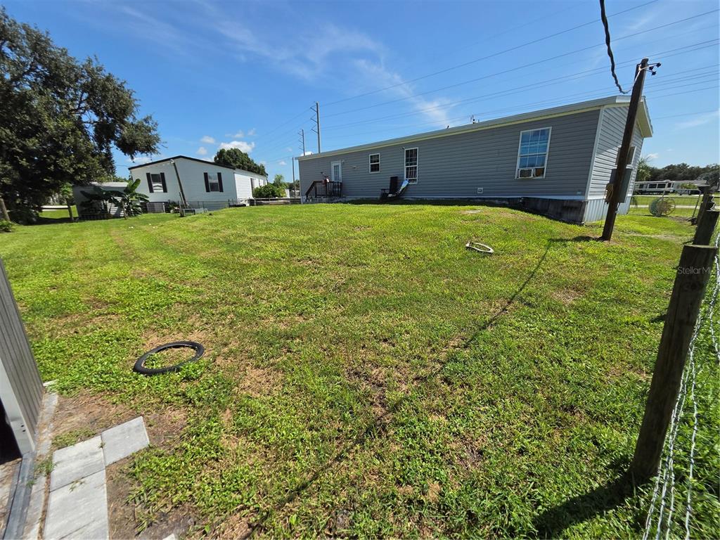A grassy backyard features a gray manufactured home and a neighboring house under a blue sky — 1837 BLOSSOM COURT, PUNTA GORDA, FL
