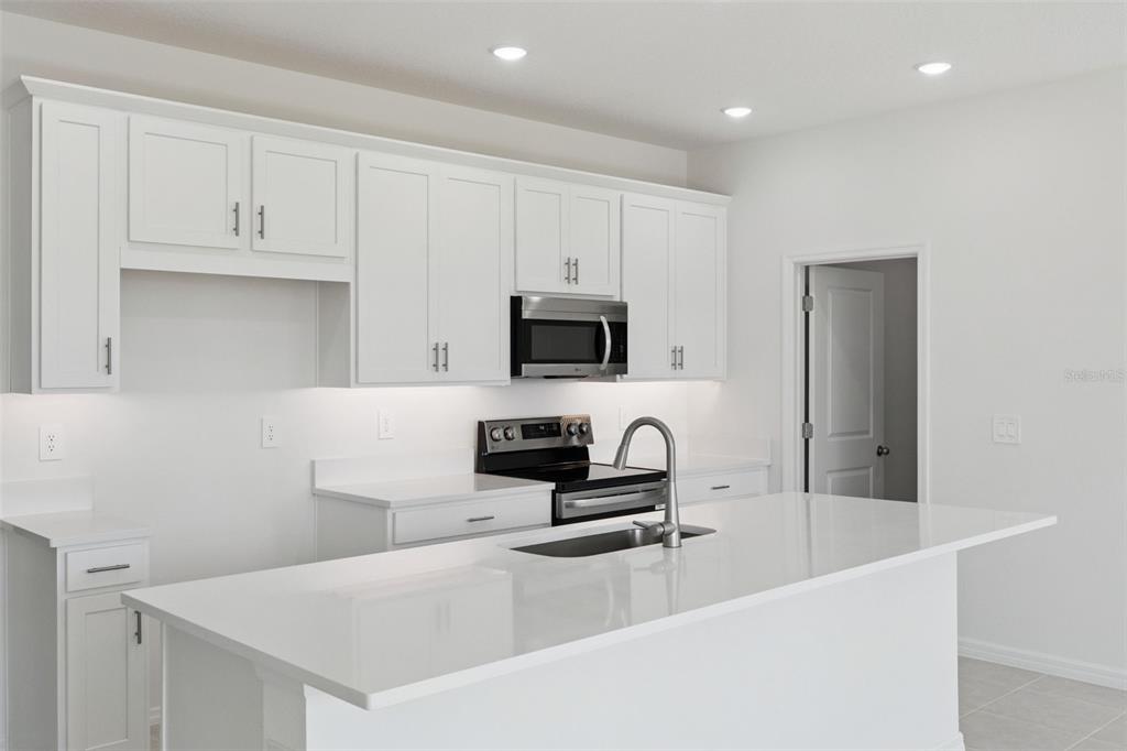 A modern kitchen features white cabinets, quartz countertops, a center island, and stainless steel appliances — 826 EMERALD GROVE DRIVE, APOPKA, FL
