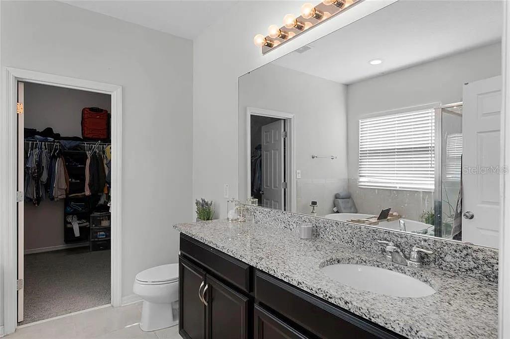 A bathroom features a dark wood vanity with a granite countertop and a large mirror — 3946 WIND DANCER CIRCLE, ST CLOUD, FL