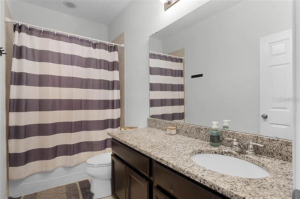 A bathroom features a granite vanity, dark cabinets, and a gray-and-white striped shower curtain — 3946 WIND DANCER CIRCLE, ST CLOUD, FL