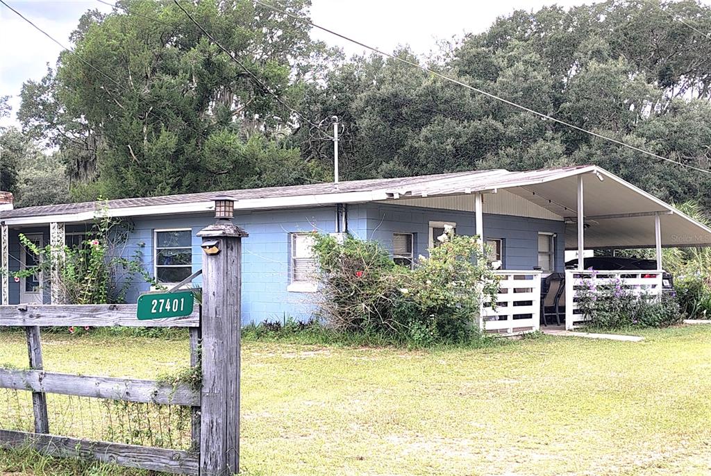 A blue, single-story concrete block house features a front porch and a wooden fence — 27401 MAIN AVENUE, OKAHUMPKA, FL
