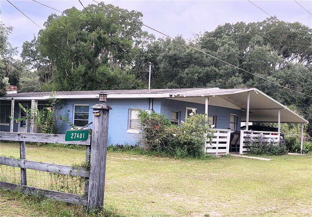 A blue, single-story house with a carport sits behind a wooden fence — 27401 MAIN AVENUE, OKAHUMPKA, FL