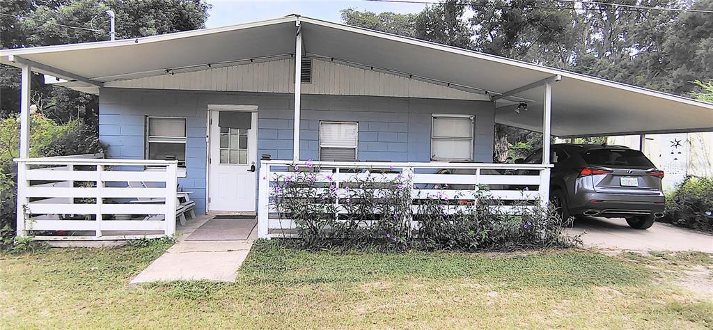 A single-story blue concrete block house features a front porch, carport, and white fencing — 27401 MAIN AVENUE, OKAHUMPKA, FL