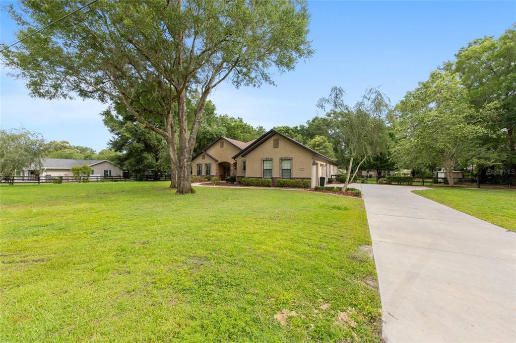 A tan single-story house with a concrete driveway sits on a large grassy lot — 3 HIALEAH DRIVE, OCALA, FL