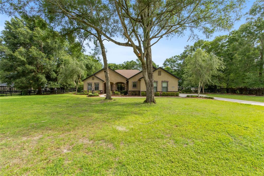 A single-story house with a tan stucco exterior sits behind two large trees on grass — 3 HIALEAH DRIVE, OCALA, FL