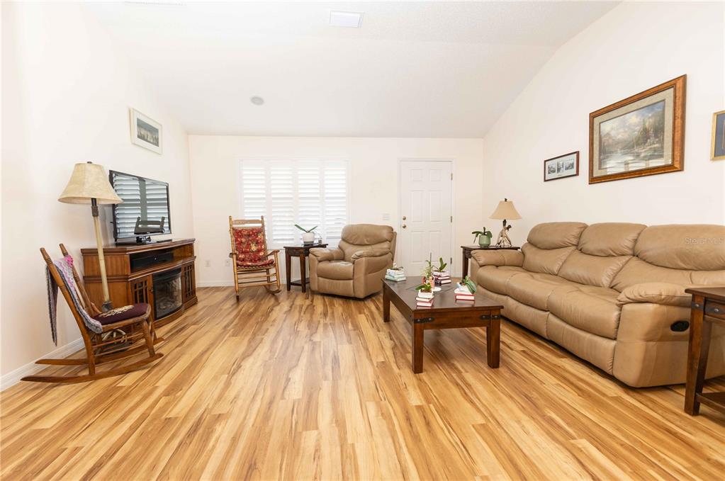 A living room features wood-look flooring, a television console, two rocking chairs, and plantation shutters — 2706 MORVEN PARK WAY, THE VILLAGES, FL