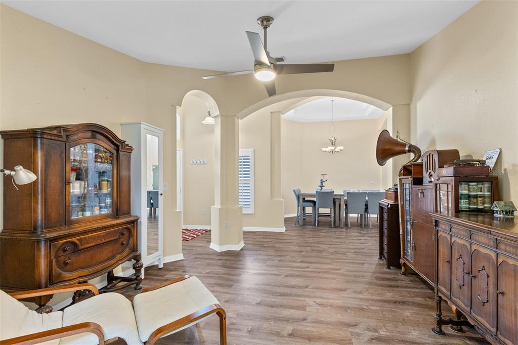 A living area with wood-look flooring, arched entryways, and antique wooden furniture leads to a dining room — 216 TAVESTOCK LOOP, WINTER SPRINGS, FL