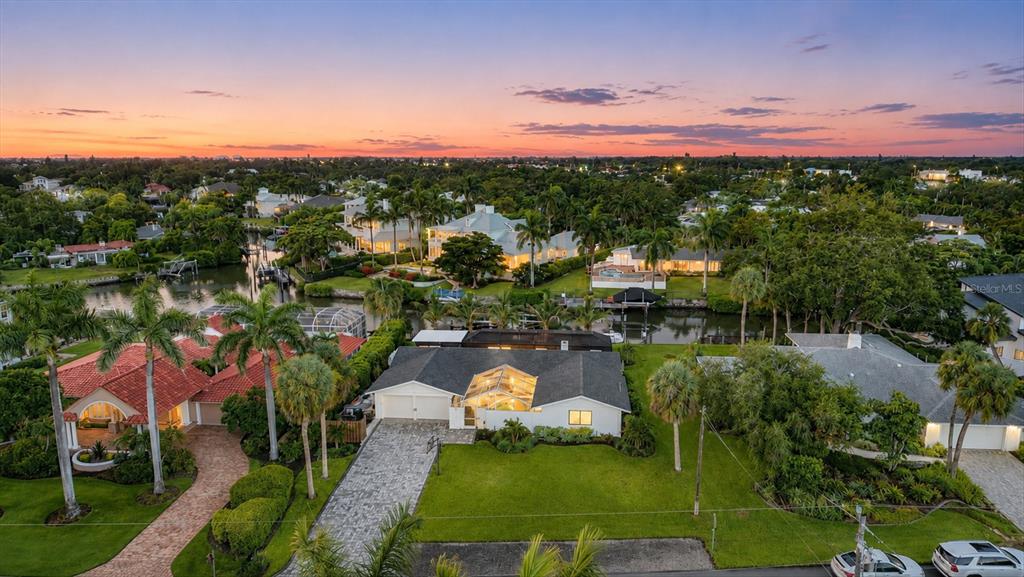 An aerial view of a suburban neighborhood featuring houses with pools and a canal at sunset — 1761 SANDALWOOD DRIVE, SARASOTA, FL