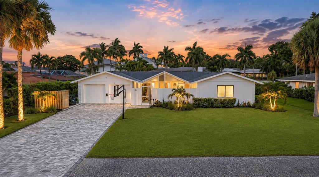 A single-story white house with a paved driveway, a basketball hoop, and palm trees at sunset — 1761 SANDALWOOD DRIVE, SARASOTA, FL