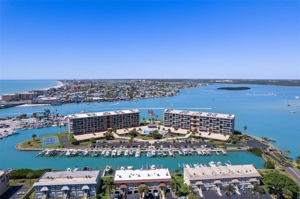 An aerial view shows two large residential buildings situated on a waterfront property with boat slips — 1 KEY CAPRI UNIT 102E, TREASURE ISLAND, FL