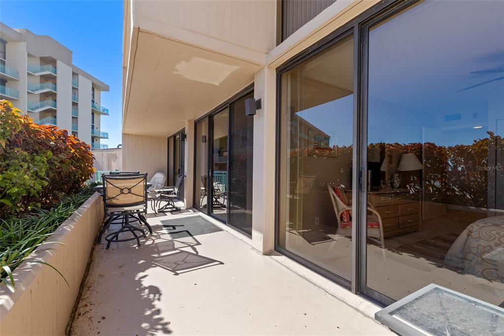 A balcony with patio furniture overlooks a neighboring building and lush landscaping — 1 KEY CAPRI UNIT 102E, TREASURE ISLAND, FL
