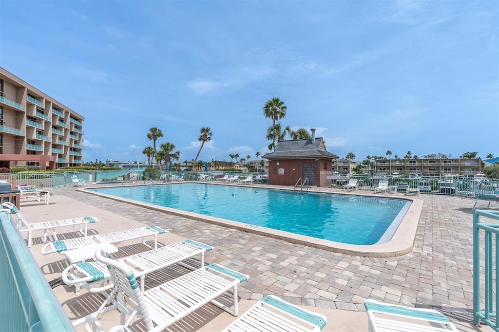 A rectangular swimming pool sits on a paved deck surrounded by lounge chairs and buildings — 1 KEY CAPRI UNIT 102E, TREASURE ISLAND, FL