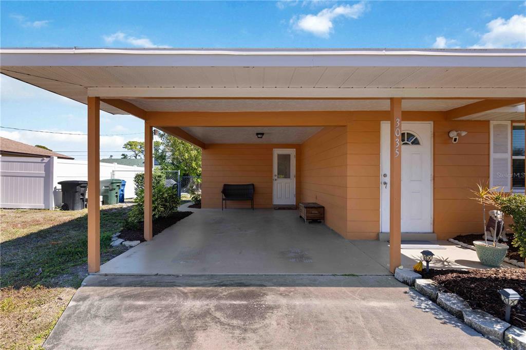 A concrete carport with a bench and a white front door on a house exterior — 3035 SHAMROCK DRIVE, VENICE, FL