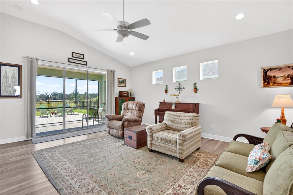A living room with a vaulted ceiling, ceiling fan, sliding glass doors, and a piano — 12923 RAINWASHED LOOP, PARRISH, FL