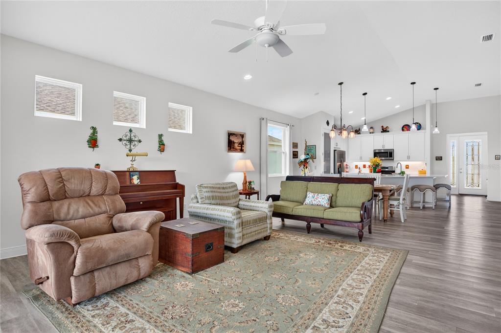 A living room with a brown recliner, patterned armchair, green sofa, and an open kitchen — 12923 RAINWASHED LOOP, PARRISH, FL
