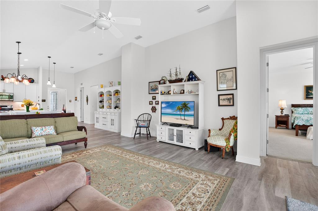 A living room features a green sofa, a television console, and an adjacent kitchen area — 12923 RAINWASHED LOOP, PARRISH, FL