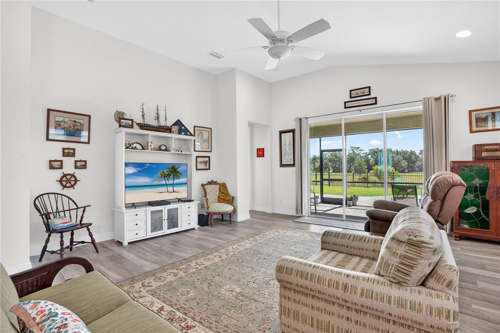 A living room features a white entertainment center, a patterned area rug, and sliding glass doors — 12923 RAINWASHED LOOP, PARRISH, FL
