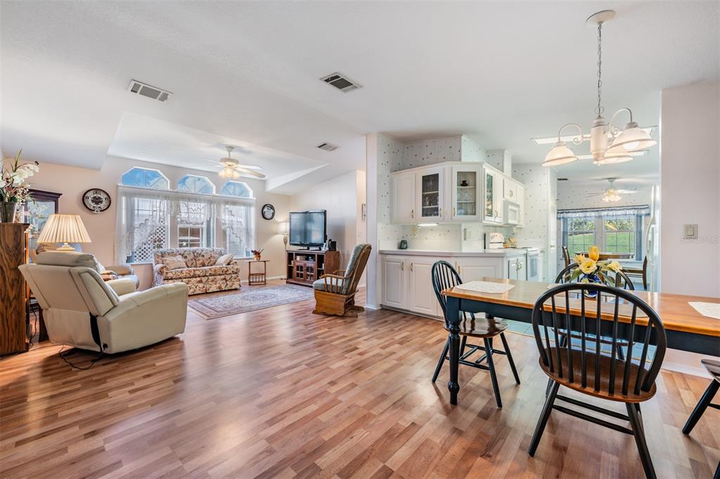 An open-concept living and dining area features wood-look flooring, white cabinetry, and large windows — 37601 NEUKOM AVENUE, ZEPHYRHILLS, FL