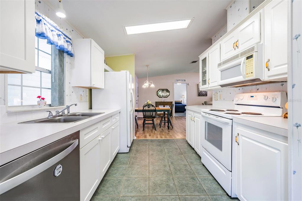 A kitchen with white cabinets, a white stove, and a sink, leading to a dining area — 37601 NEUKOM AVENUE, ZEPHYRHILLS, FL