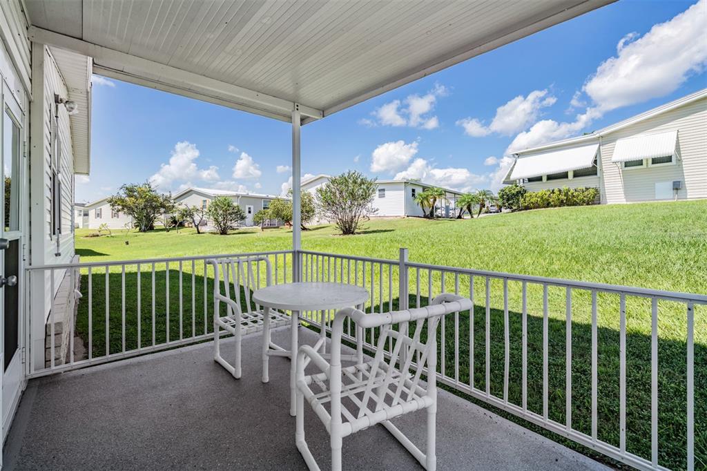 A covered concrete patio with white railings, a small table, and two chairs overlooks grass — 37601 NEUKOM AVENUE, ZEPHYRHILLS, FL