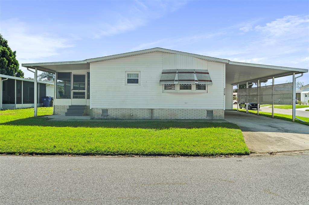 A single-story mobile home with white siding, a carport, and a screened-in front porch — 2519 INDEPENDENCE LN, ST CLOUD, FL