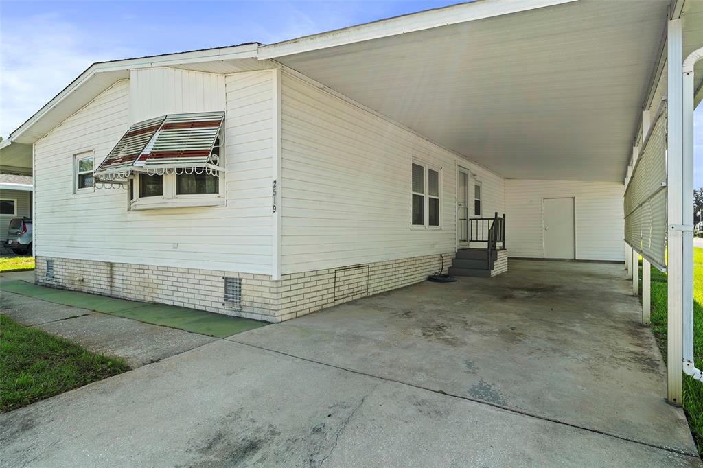A white mobile home with a carport, brick skirting, and a striped window awning — 2519 INDEPENDENCE LN, ST CLOUD, FL