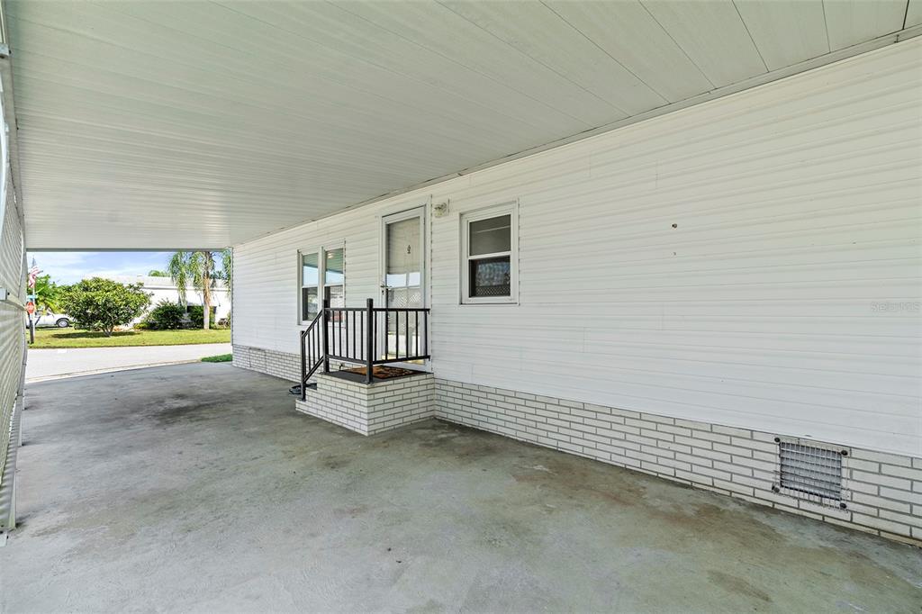 A concrete carport leads to a white-sided mobile home with a small brick-trimmed entryway — 2519 INDEPENDENCE LN, ST CLOUD, FL