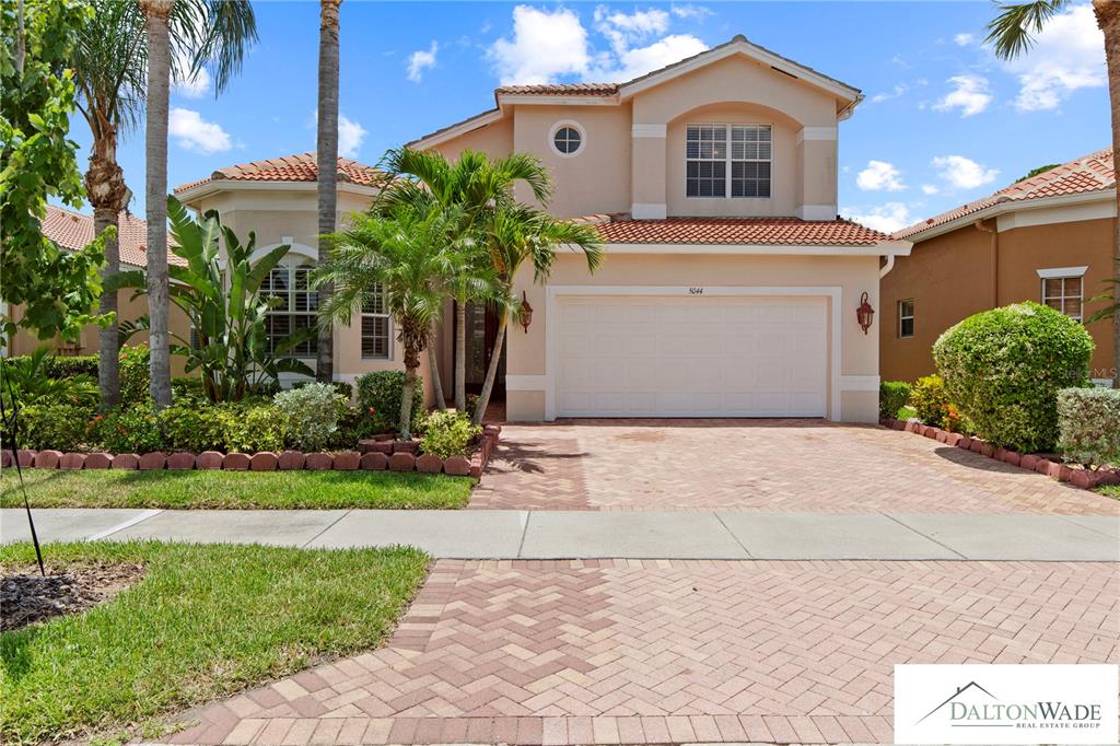 A two-story suburban house with a tan stucco exterior, tile roof, and brick paver driveway — 5044 SANDY BROOK CIRCLE, WIMAUMA, FL