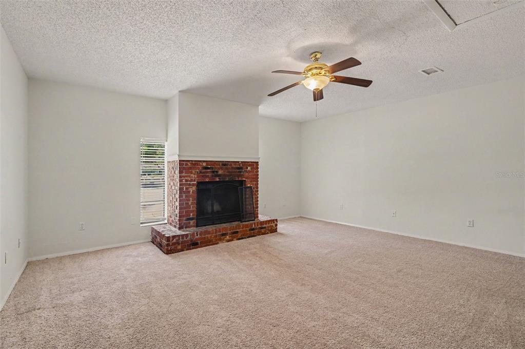 A living room with beige carpet, white walls, a ceiling fan, and a brick fireplace — 510 WAVECREST DRIVE, ORLANDO, FL