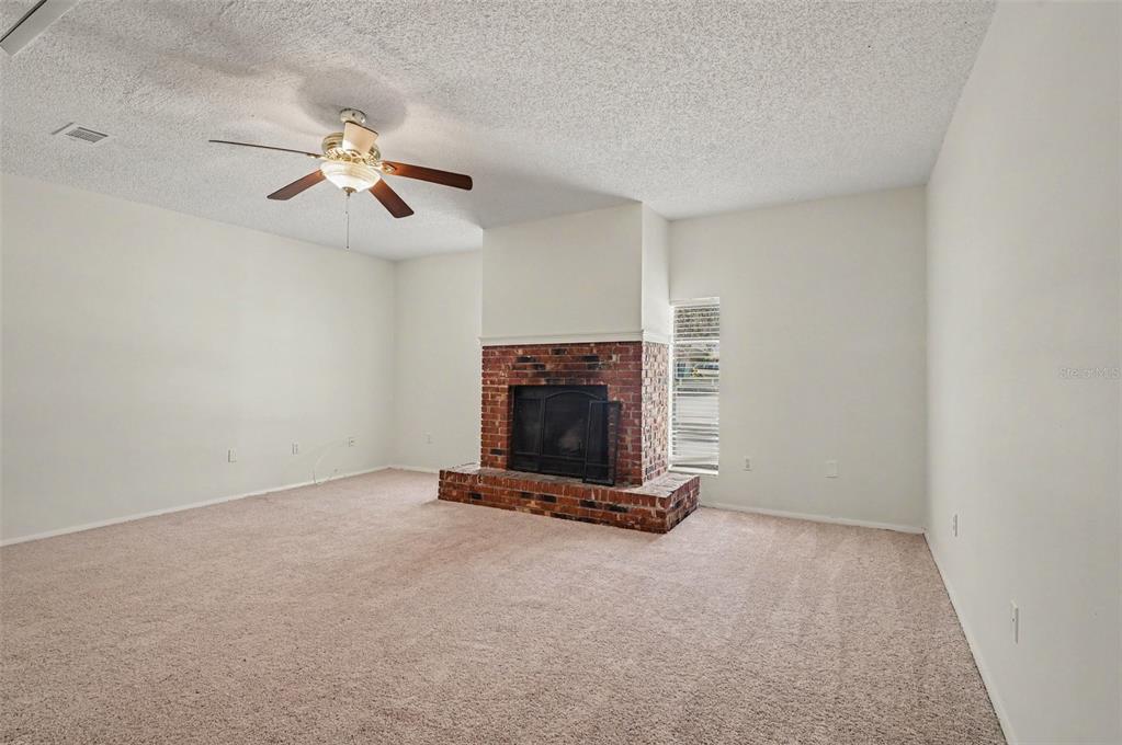 A living room features beige carpeting, white walls, a ceiling fan, and a brick fireplace — 510 WAVECREST DRIVE, ORLANDO, FL